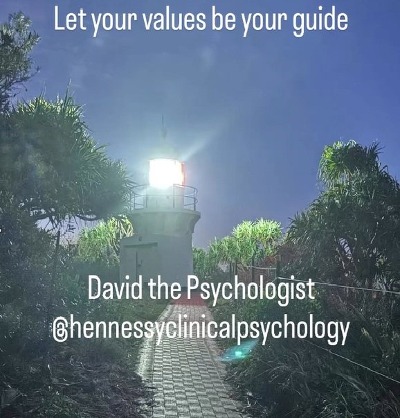 A softly illuminated lighthouse on a coastal walking path at dusk, symbolising guidance and direction. White text reads Let your values be your guide and David the Psychologist at hennessyclinicalpsychology. The scene represents how personal values can act like a guiding light during emotional or uncertain times.