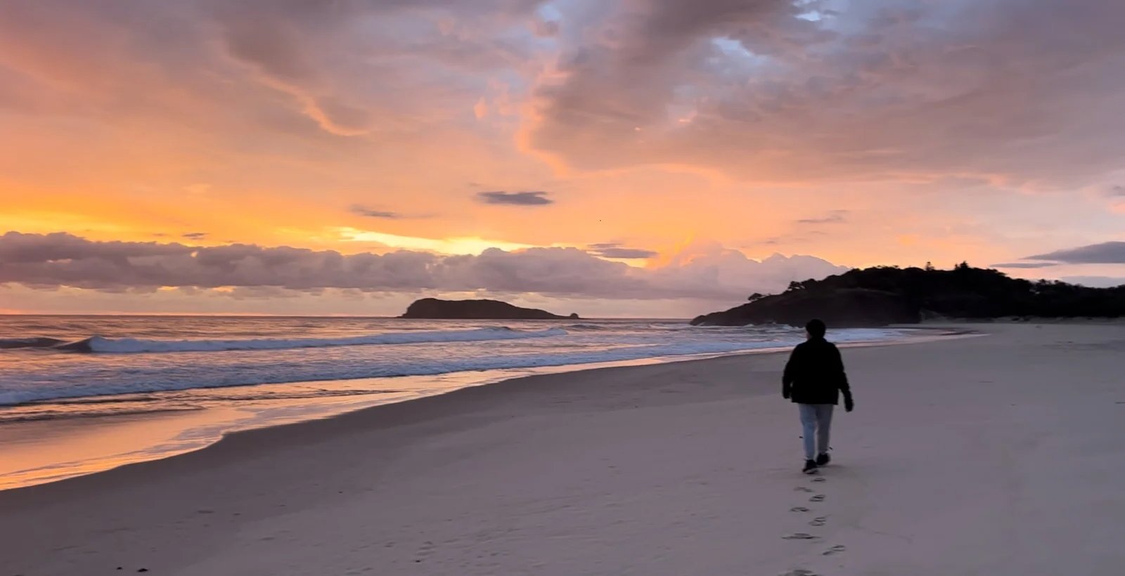 Man walking along the beach at sunrise