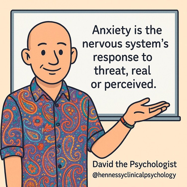 Cartoon of David the Psychologist standing beside a whiteboard with the words Anxiety is the nervous system response to threat real or perceived. David is bald, wearing a colourful paisley shirt and a bead bracelet with one red and one green bead. Subtle text reads David the Psychologist at hennessyclinicalpsychology.