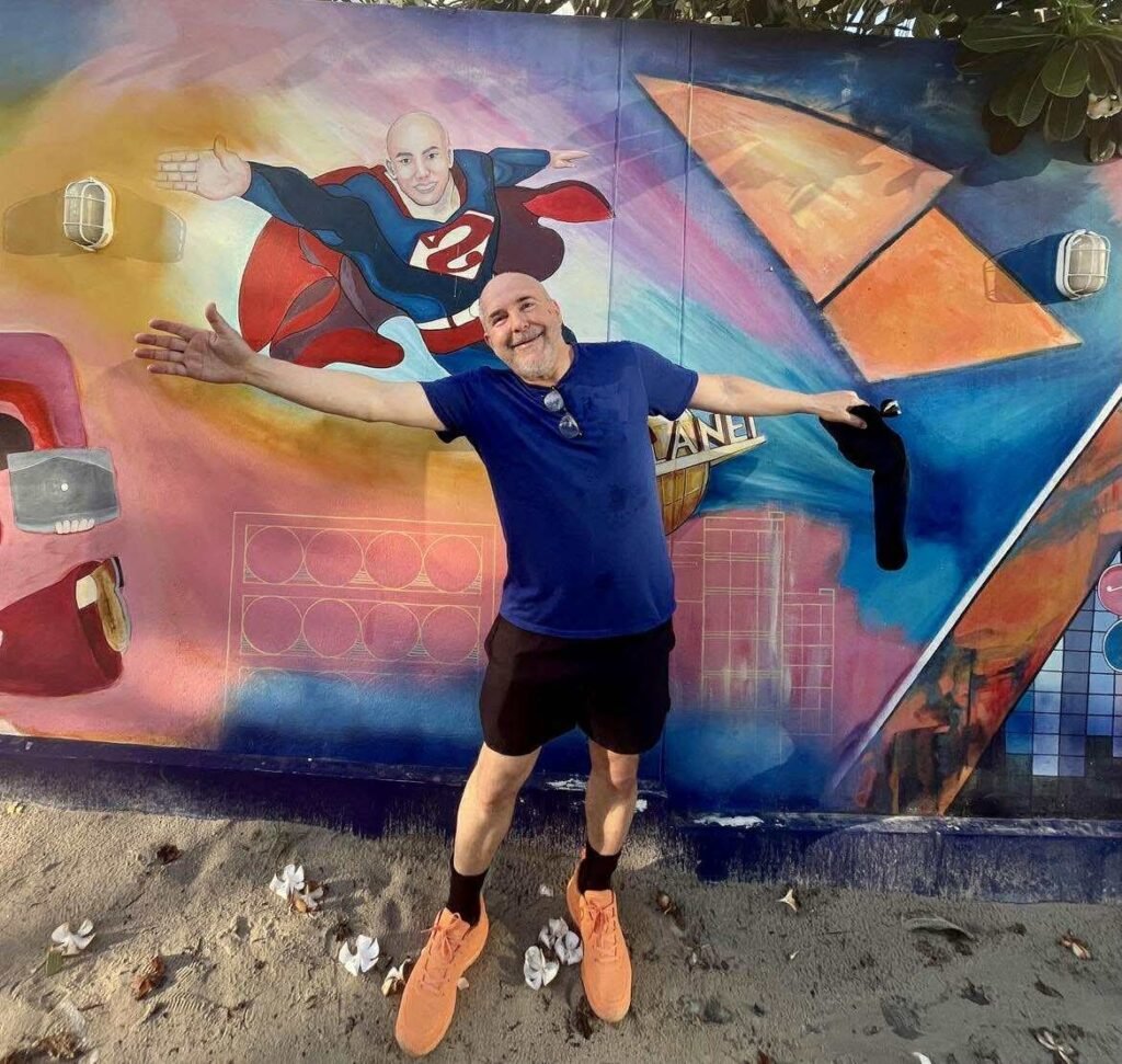 Thoughts are not facts | David the Psychologist smiling with arms outstretched in front of a mural showing a superhero version of himself.