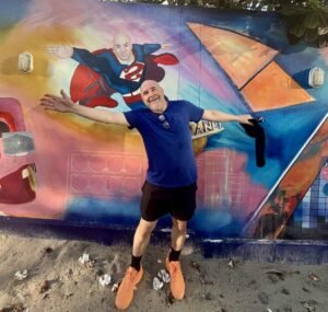 Thoughts are not facts | David the Psychologist smiling with arms outstretched in front of a mural showing a superhero version of himself.