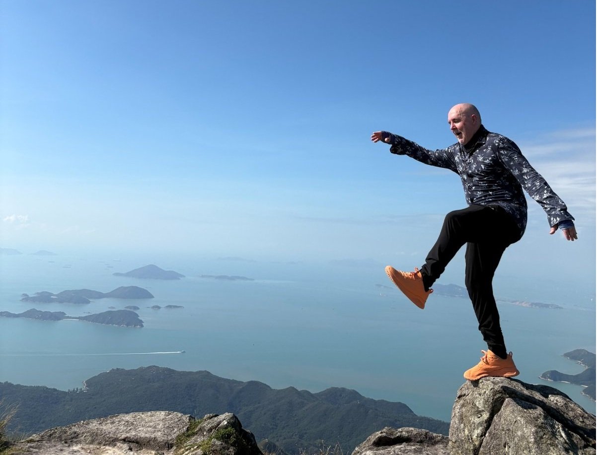 David the Psychologist balancing on a mountain peak under a clear blue sky, symbolising mindfulness, perspective, and balance when responding to the inner critic.
