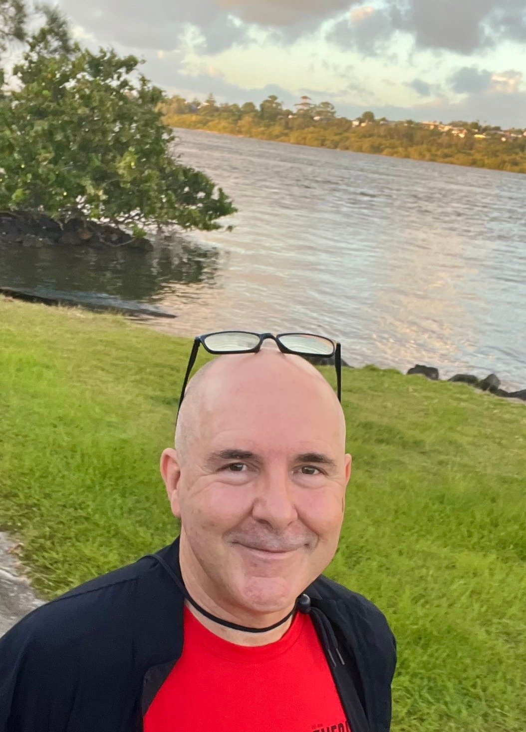 Clinical Psychologist for NDIS Participants | David Hennessy, a clinical psychologist, smiling outdoors beside a river at sunset, representing a calm and supportive approach to NDIS capacity building psychology.