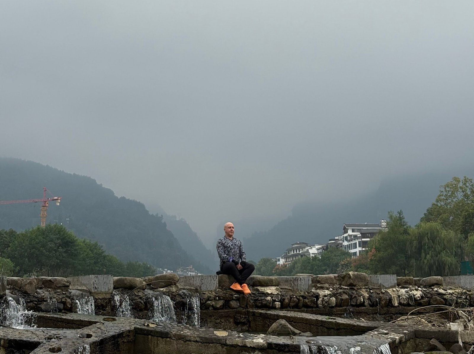 The Irony of Attachment | David the Psychologist sits calmly beside flowing water and misty mountains, representing the irony of attachment — seeking stability while learning to release grasping through awareness and balance.