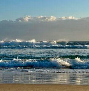 Ocean waves rolling onto a quiet beach under a clear sky, symbolising slowing down, intentional effort, and long-term mental wellbeing