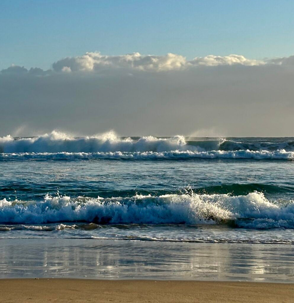 Ocean waves rolling onto a quiet beach under a clear sky, symbolising slowing down, intentional effort, and long-term mental wellbeing