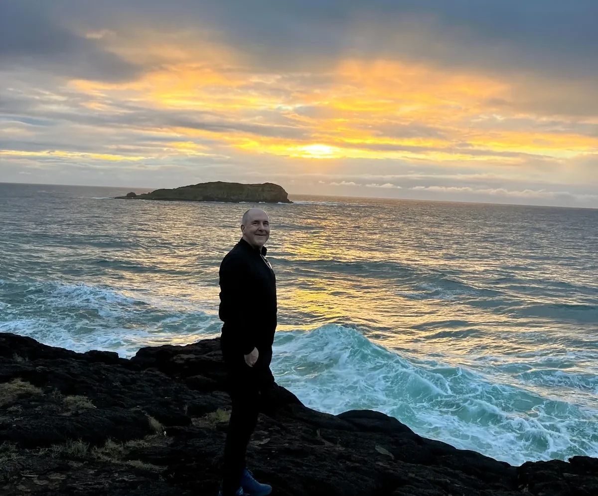 David Hennessy standing beside the ocean at sunset
