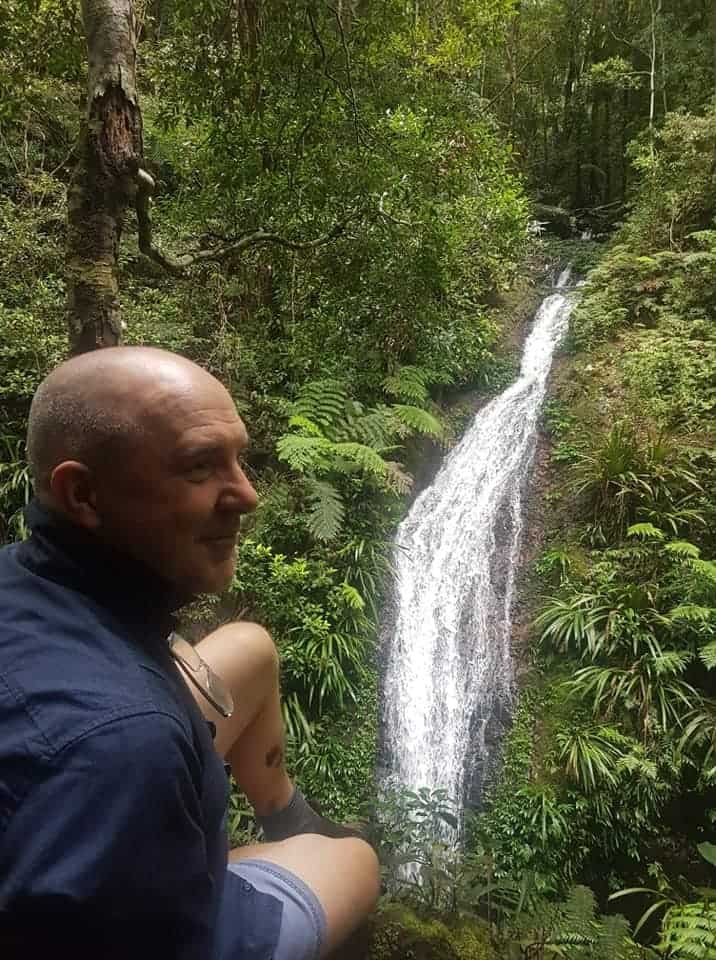 David Hennessy sitting beside a rainforest waterfall during a bushwalk, reflecting on the journey from tradesman to clinical psychologist and the value of lifelong learning.