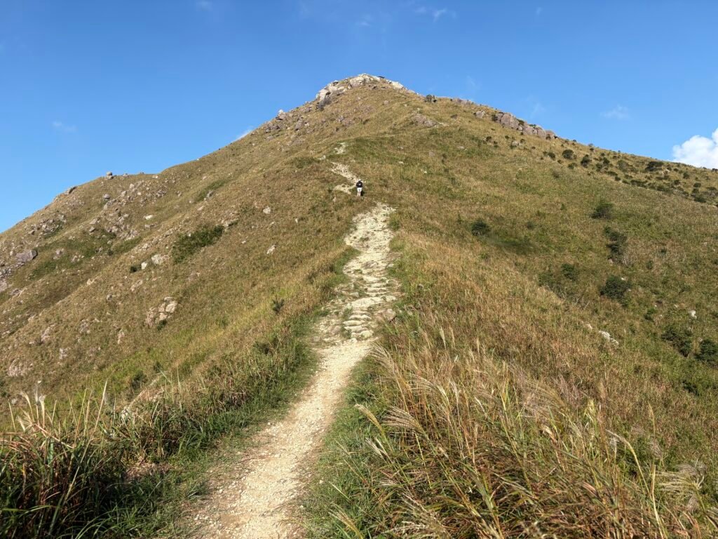 Person walking up a rocky mountain path beneath a clear blue sky