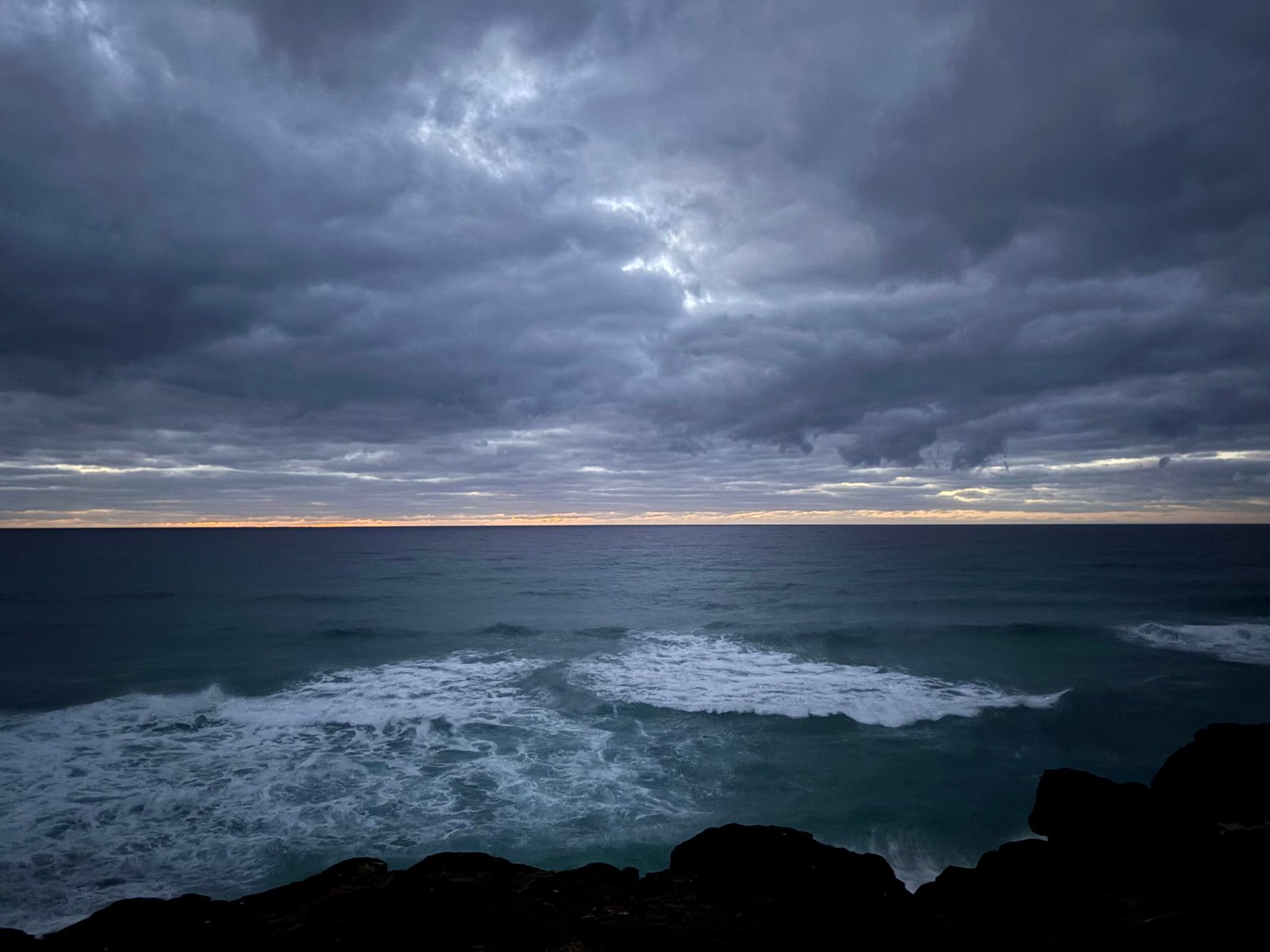 Dark storm clouds gathering over ocean waves and a rocky coastline